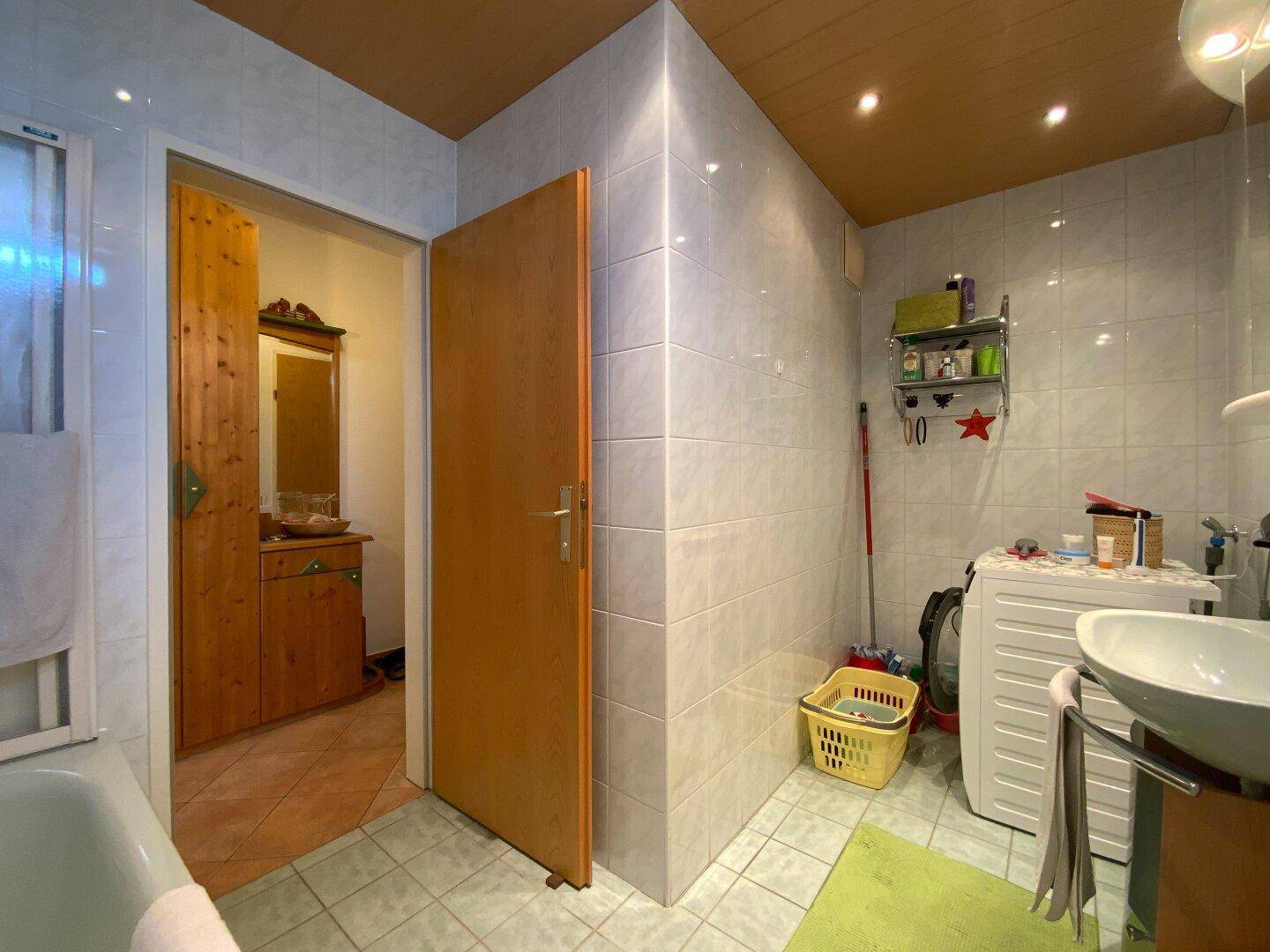 Badezimmer mit Waschbecken, Waschmaschine und hell gefliesten Wänden.