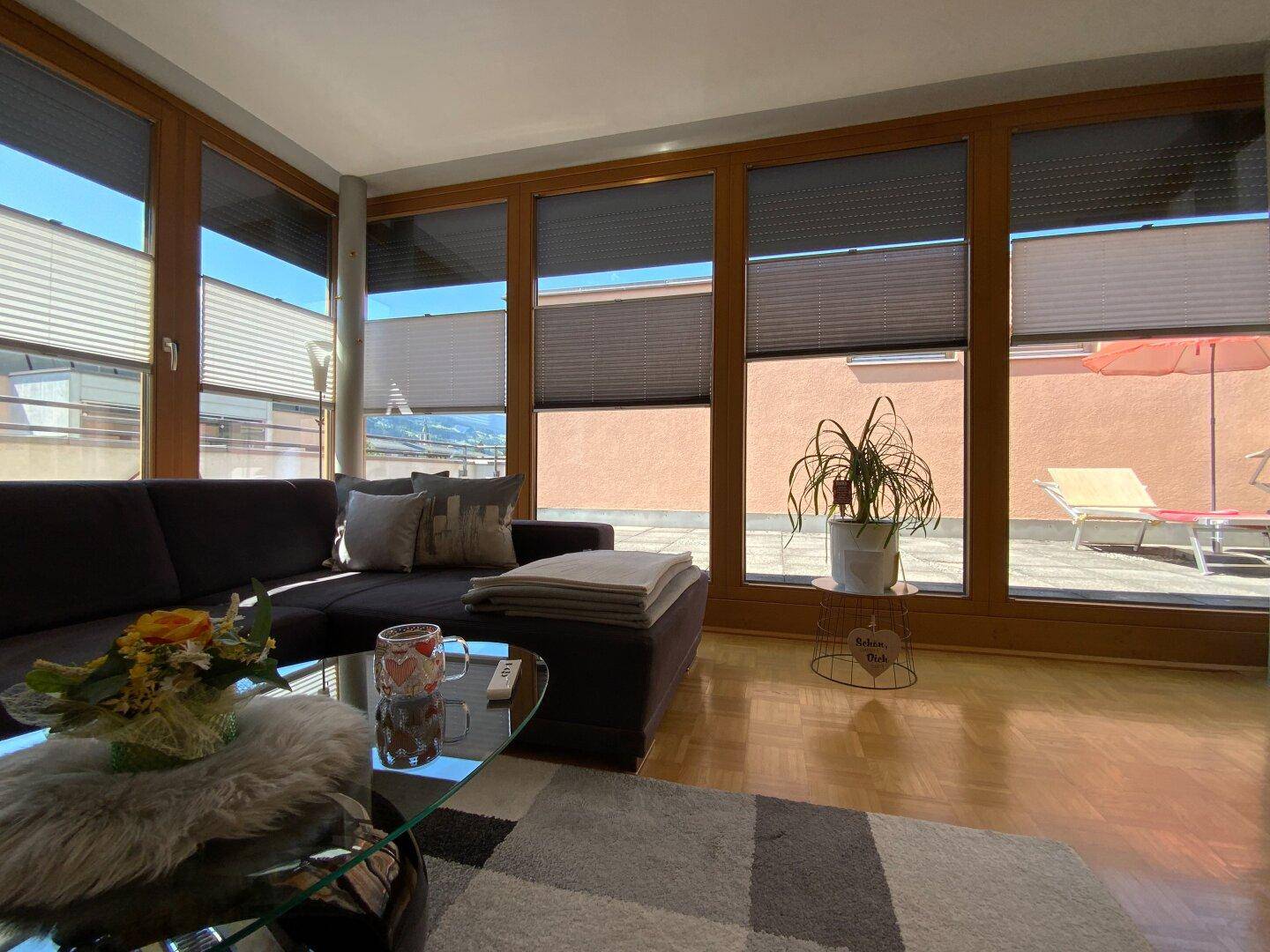 Helles Wohnzimmer mit großen Fenstern, die Zugang zur Terrasse bieten, und modernem Mobiliar.