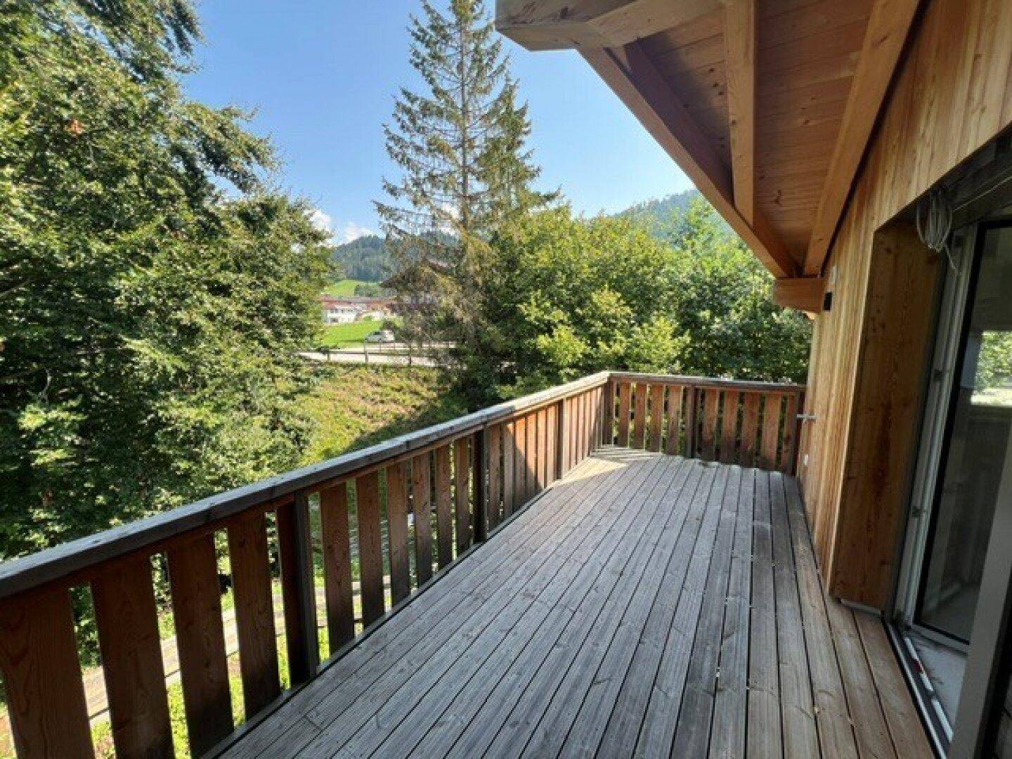 Geräumiger Holzbalkon mit Blick auf die grüne Umgebung und die Berge.