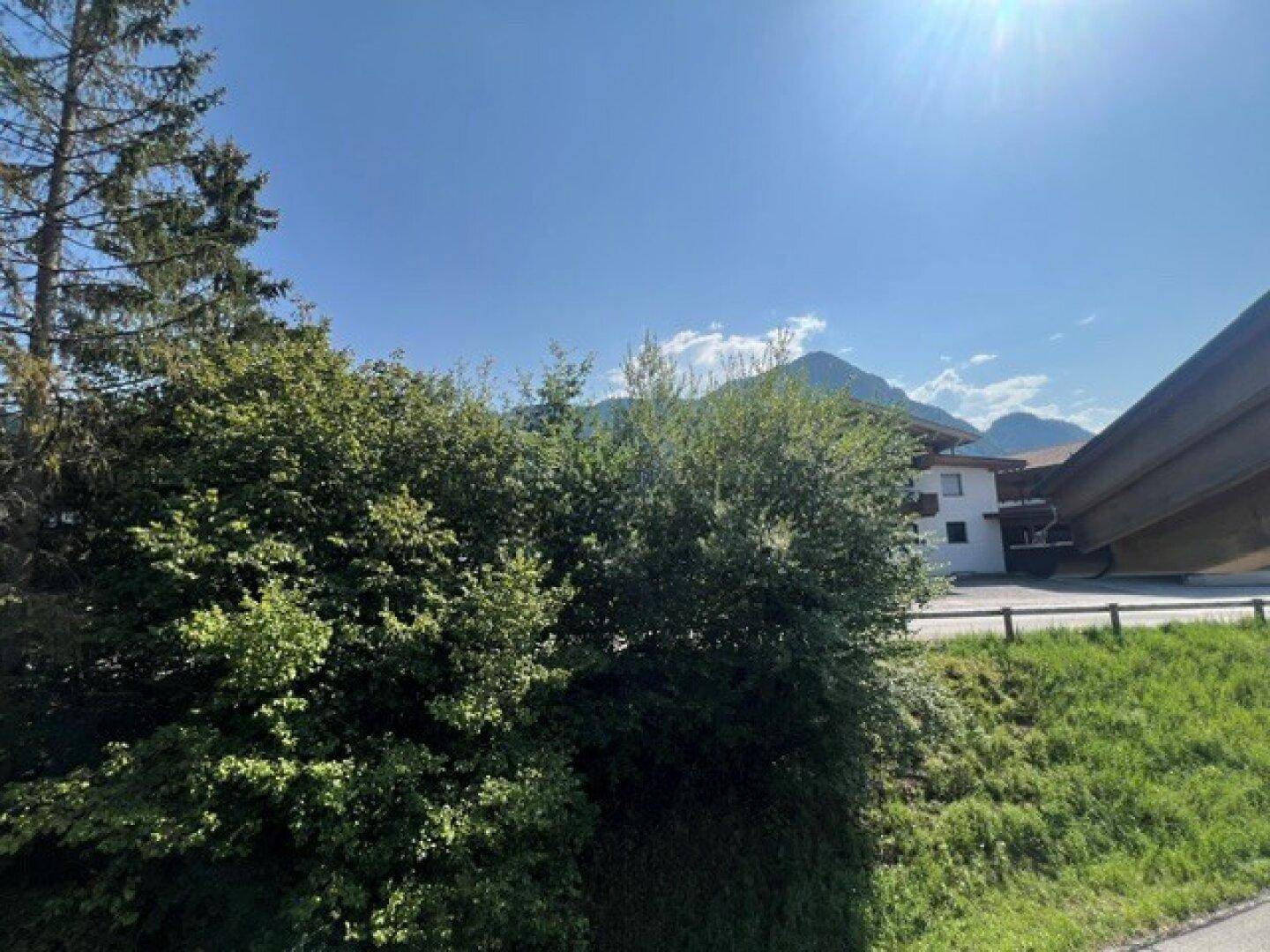 Panoramablick auf die grüne Landschaft mit Bergen und einem Gebäude im Hintergrund.