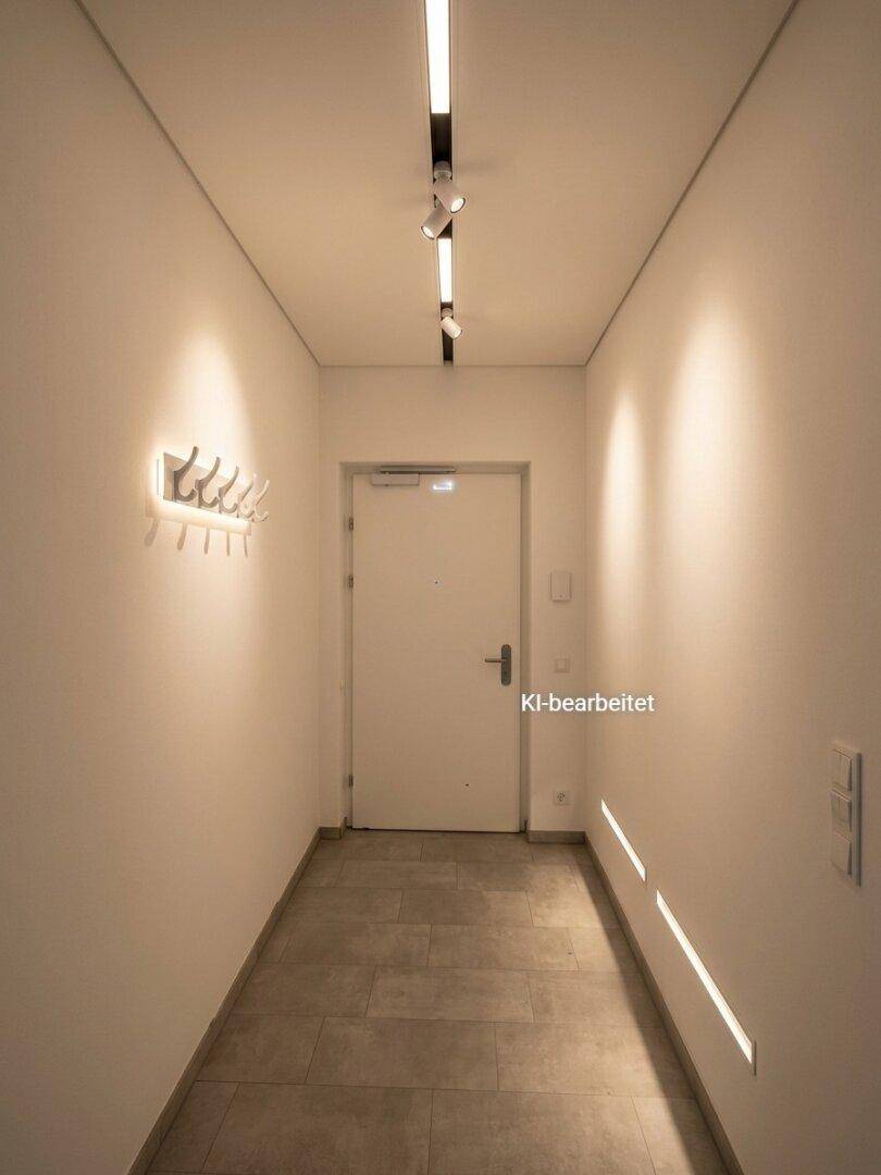Eingangsbereich mit Fliesenboden, moderner Beleuchtung und Garderobenhaken an der Wand.