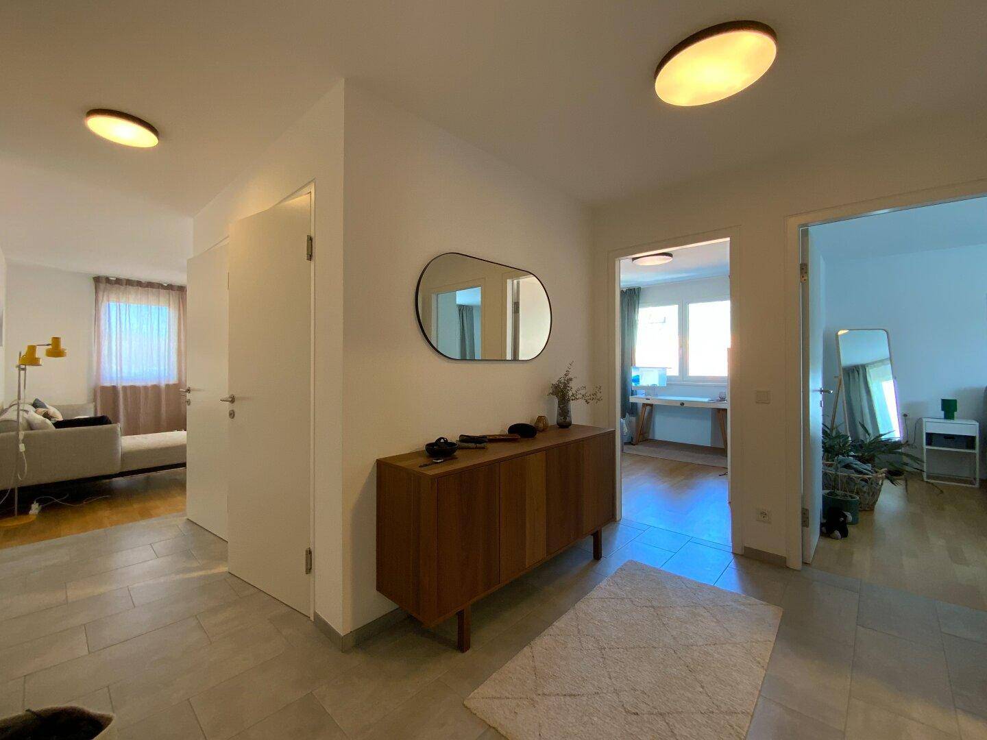 Heller Flur mit Fliesenboden, modernem Sideboard und großem Spiegel, verbindet verschiedene Räume.