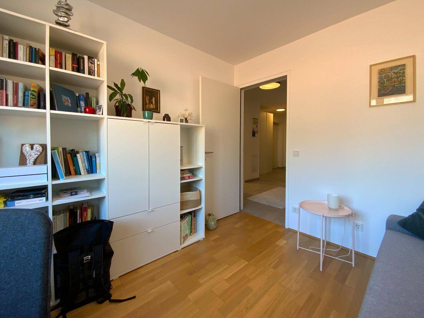 Helles Zimmer mit Bücherregal und Zugang zu einem Flur, ideal als Büro oder Gästezimmer.