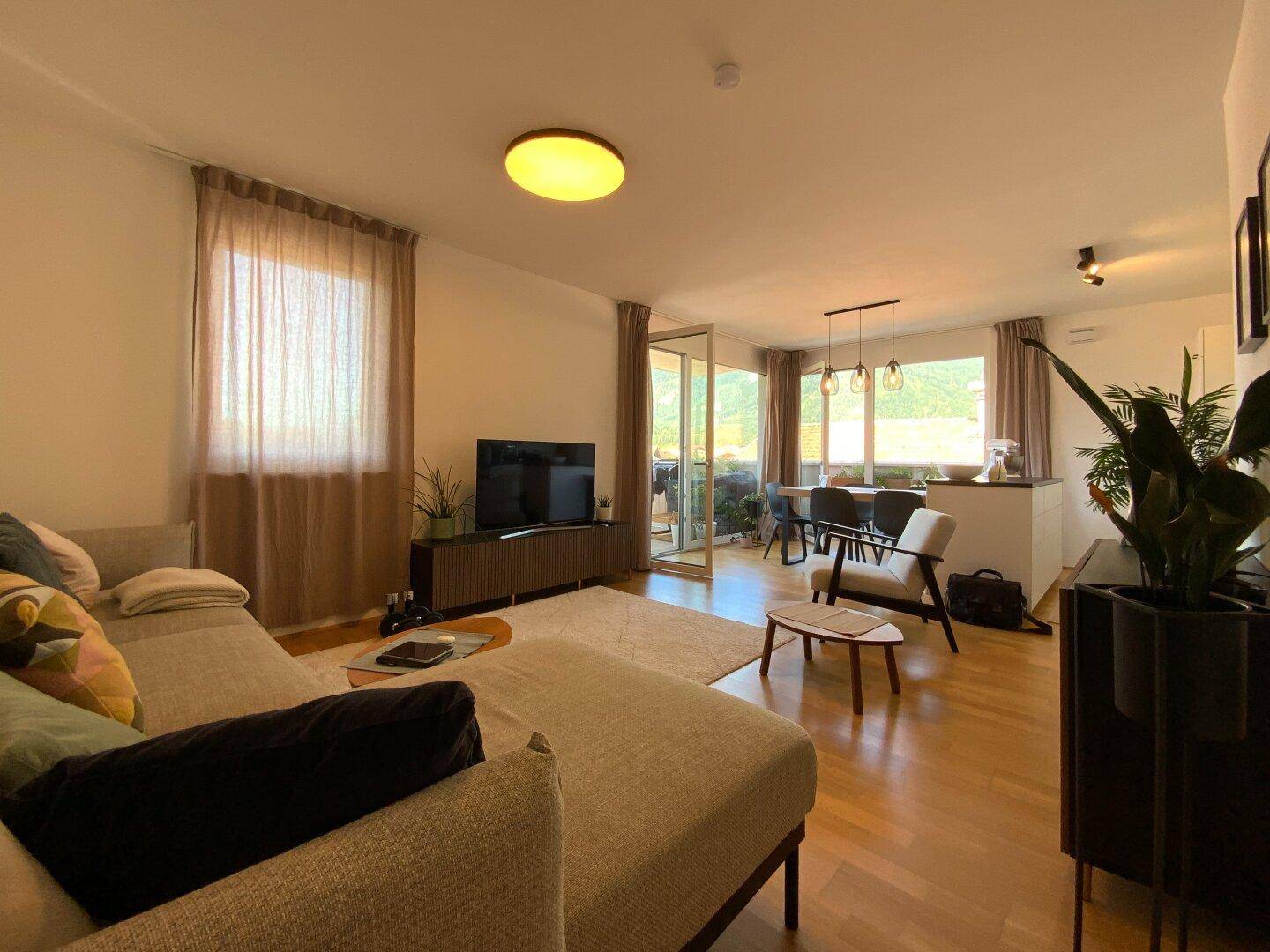Gemütliches Wohnzimmer mit Sofa, Fernseher und Blick auf den Essbereich und die Terrasse.