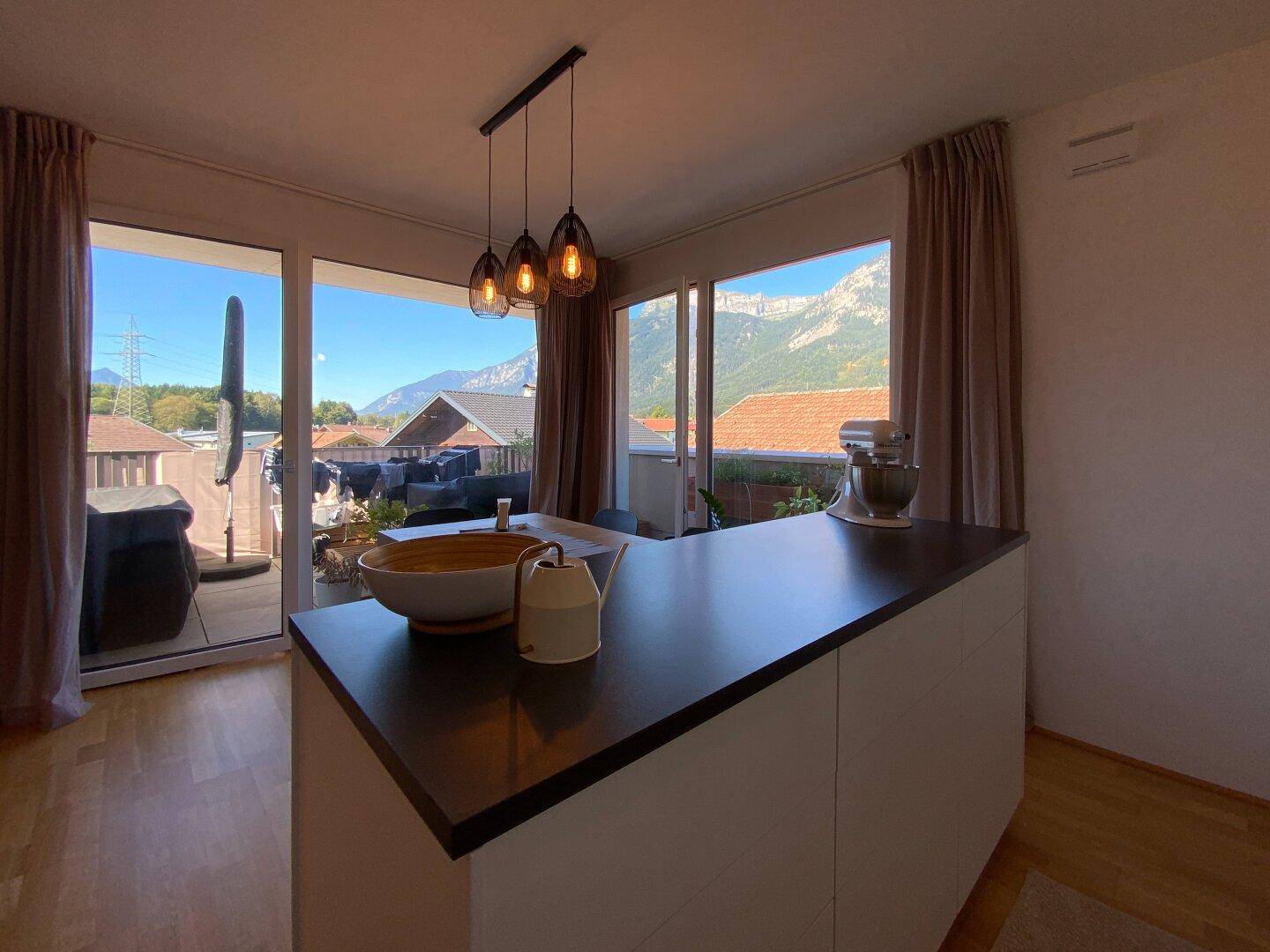 Moderne Küche mit Kochinsel und Essbereich, direktem Zugang zur Terrasse und Bergblick.