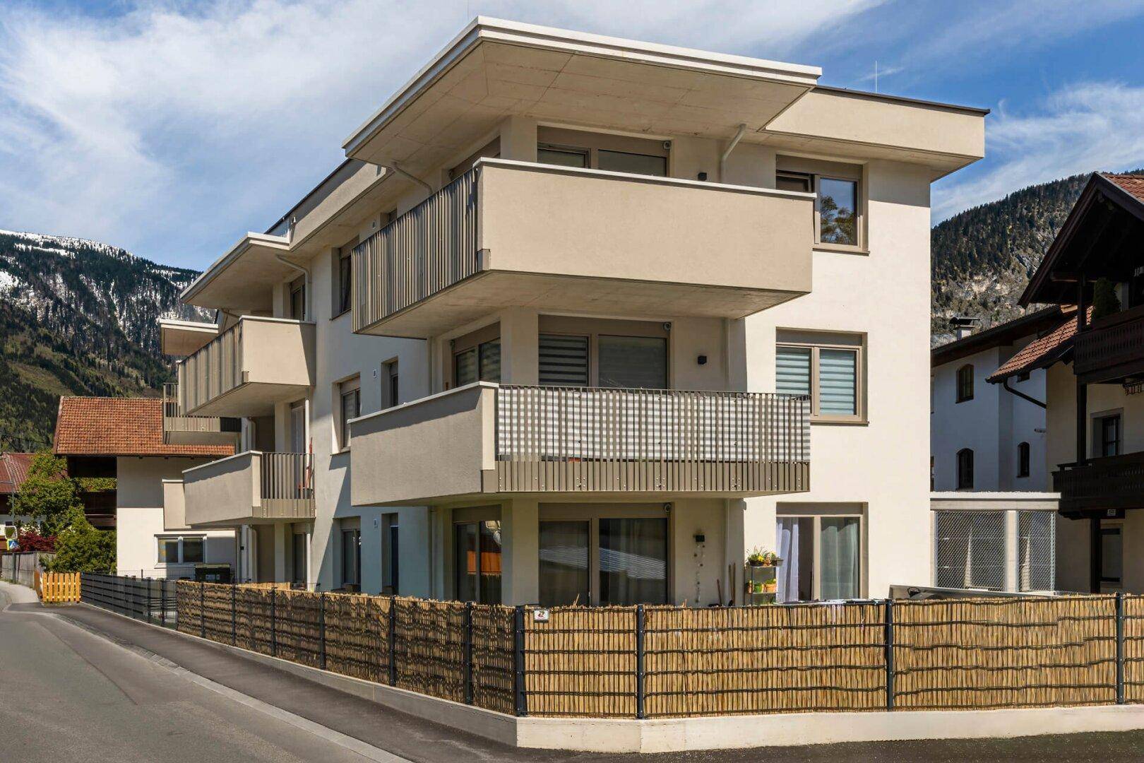 Moderne Wohnanlage mit mehreren Balkonen und heller Fassade in alpiner Umgebung.