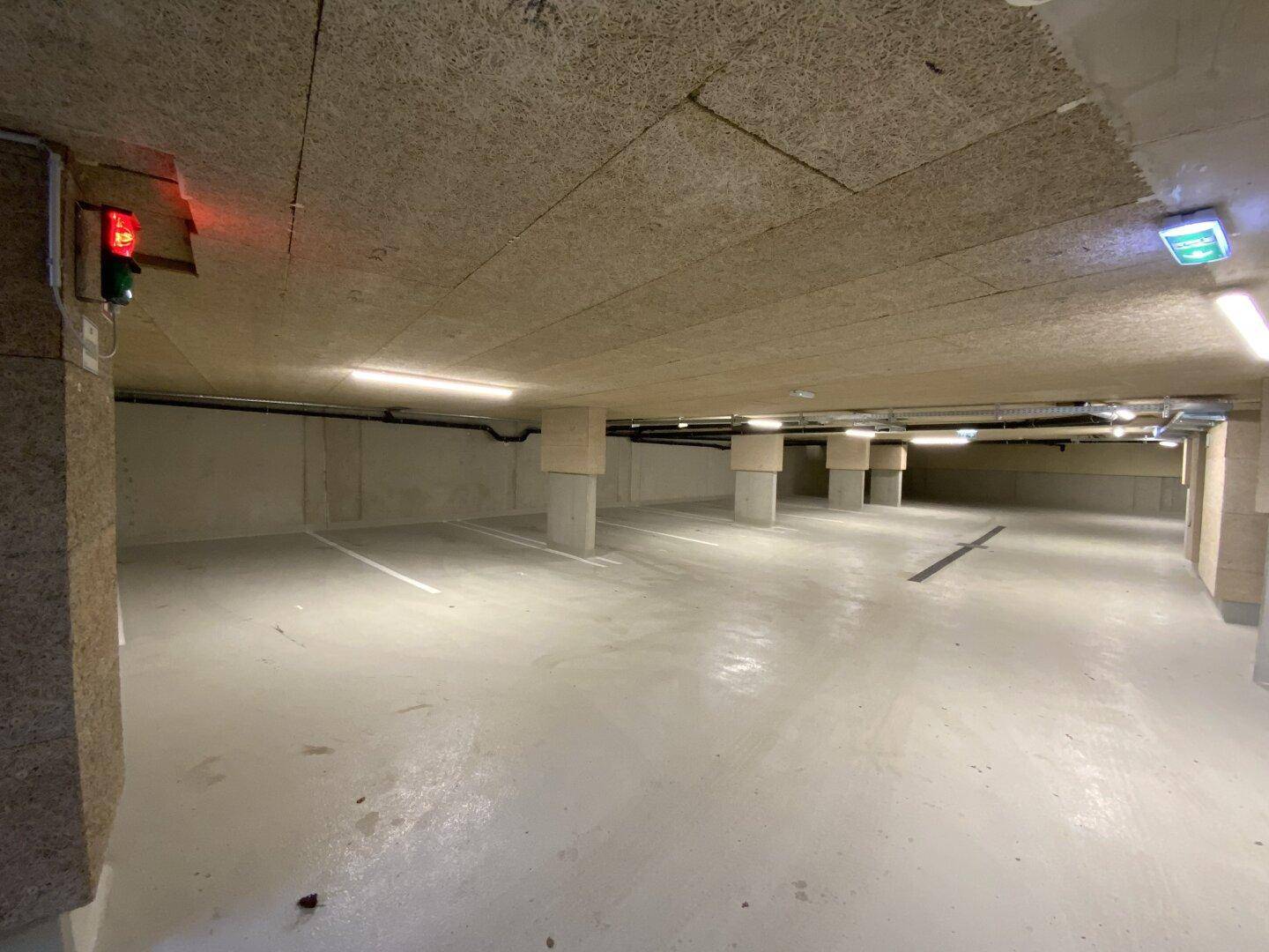 Geräumige Tiefgarage mit mehreren Stellplätzen, Betonpfeilern und heller Beleuchtung.