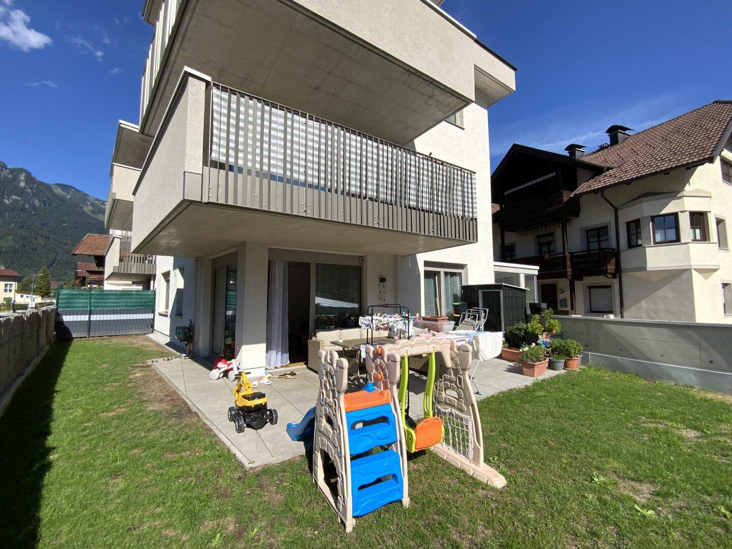 Gartenbereich mit Rasenfläche, Kinderspielgeräten und Blick auf die umliegenden Berge.