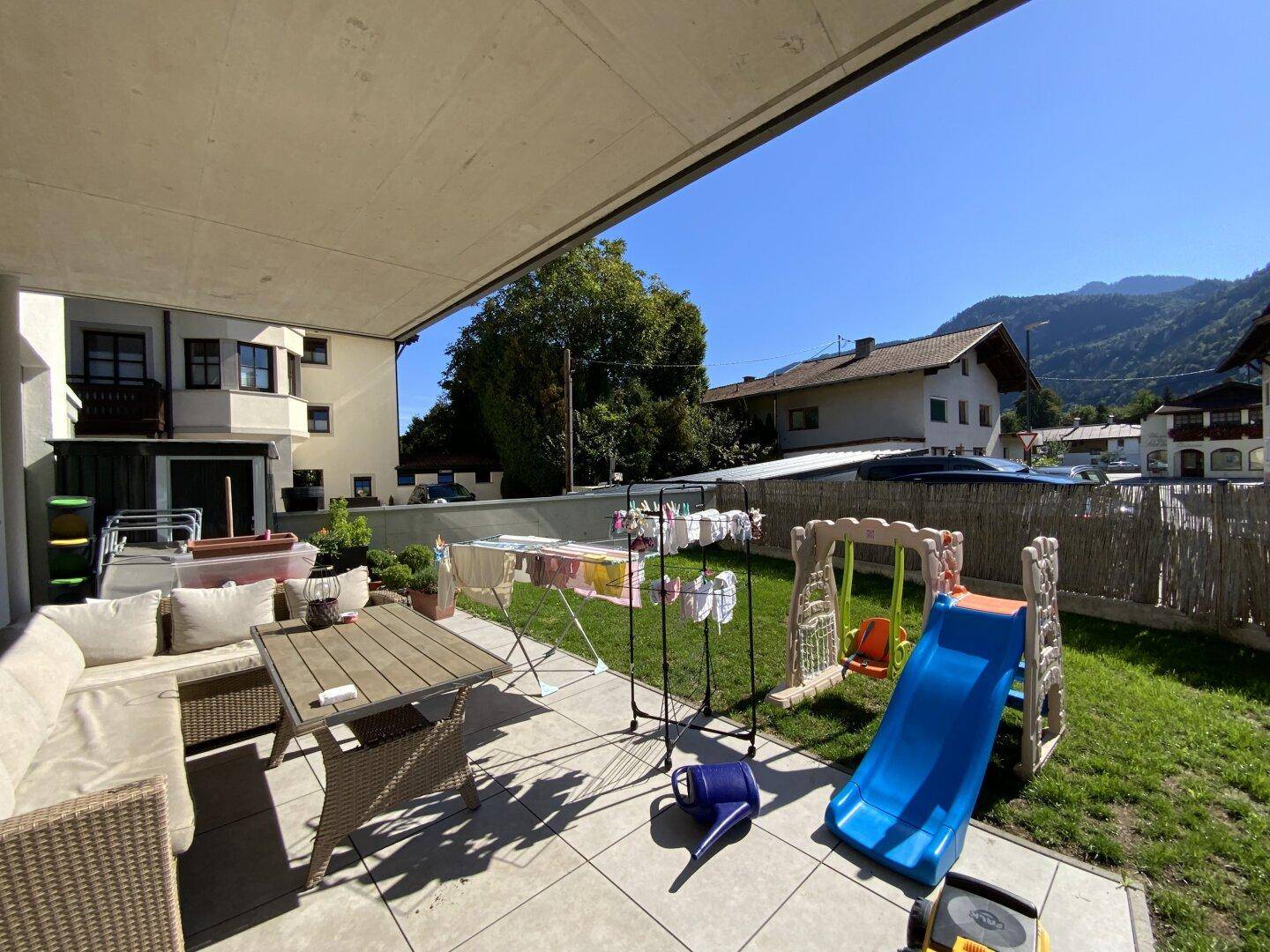 Sonniger Terrassenbereich mit Sitzgelegenheiten, Spielgeräten und Bergblick.