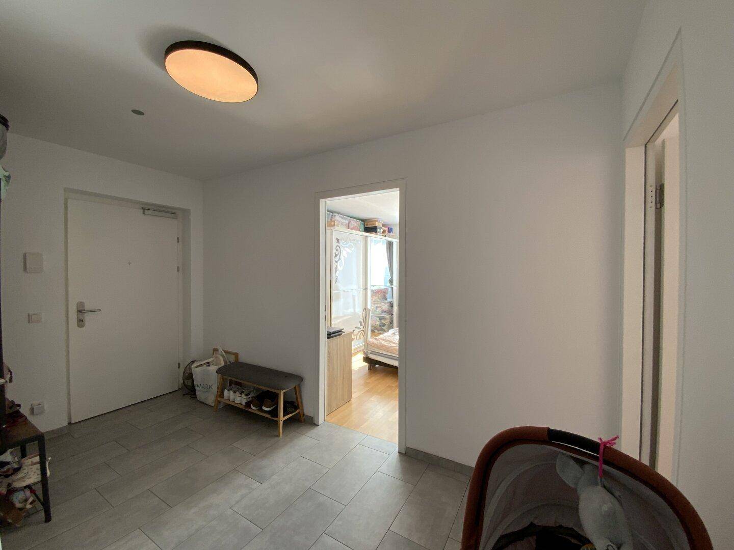 Eingangsbereich mit Fliesenboden, Schuhbank und Blick in angrenzende Zimmer.