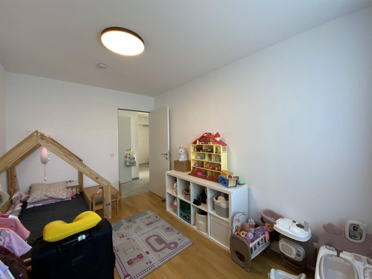 Kinderzimmer mit Holzboden, Spielzeug und einem kleinen Hausbett.