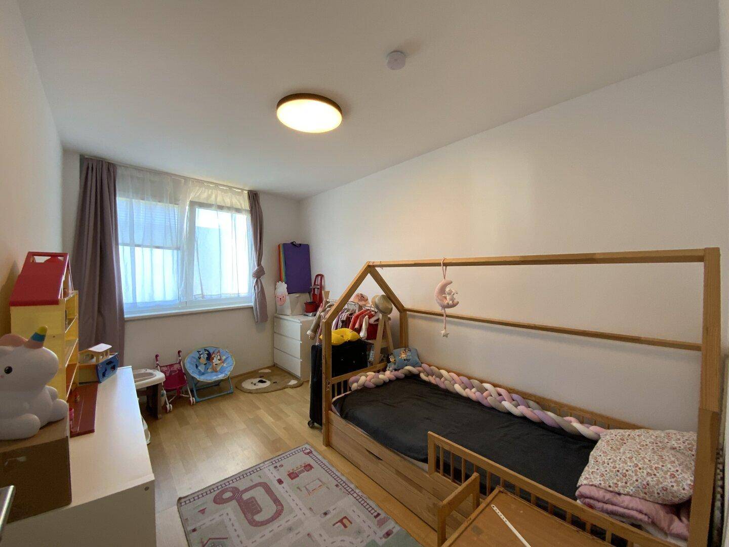 Helles Kinderzimmer mit Holzboden, Fenster und Spielbereich.