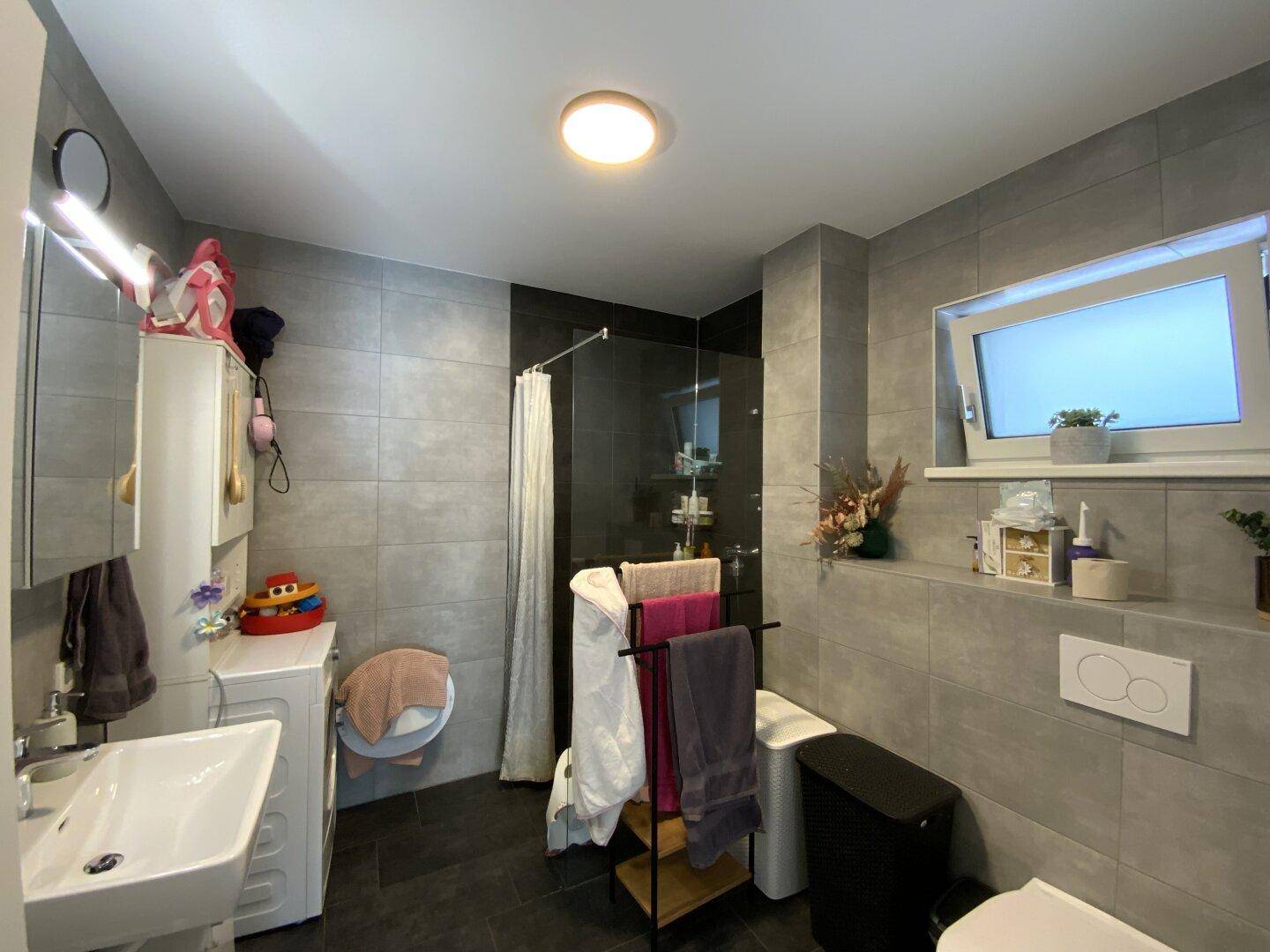 Zeitgemäßes Badezimmer mit Dusche, WC, Waschmaschine und Fenster.