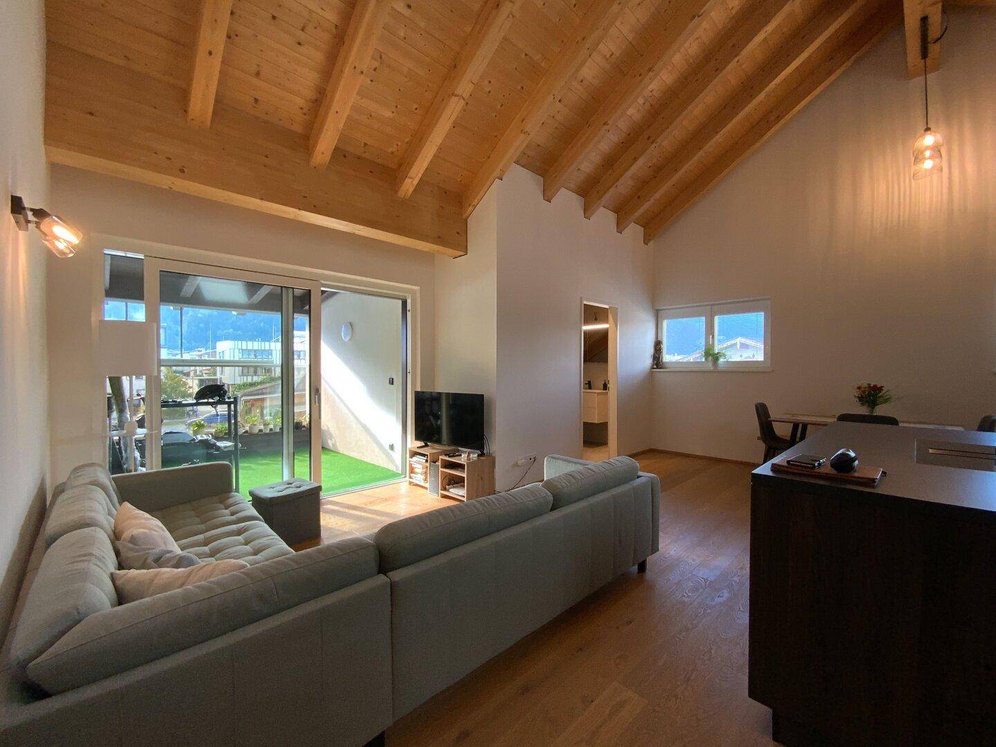 Heller Wohnbereich mit großem Sofa, Zugang zur Terrasse und Blick auf die Umgebung.