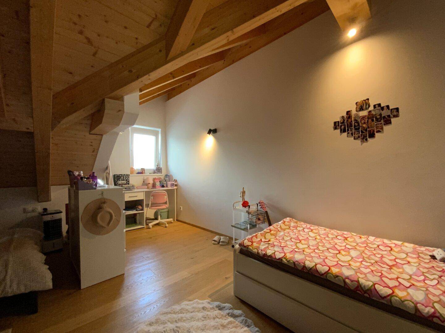 Kinderzimmer mit Holzbalkendecke, Dachschräge und hellem Arbeitsbereich am Fenster.