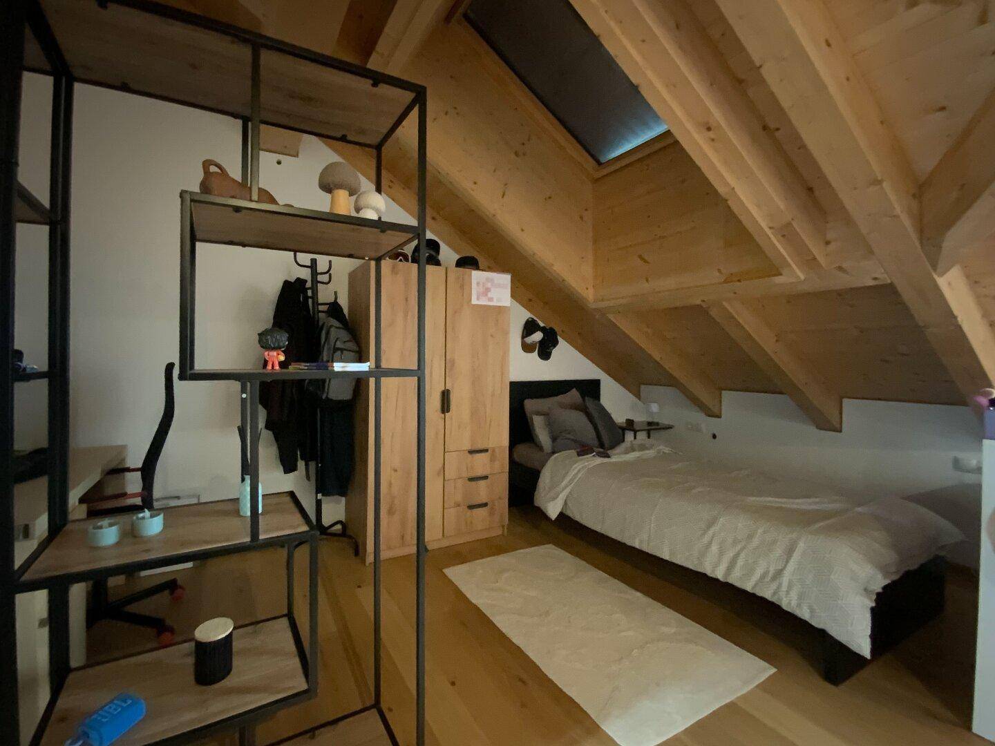 Gemütliches Schlafzimmer mit Holzbalkendecke, Dachschräge und Dachfenster für natürliches Licht.