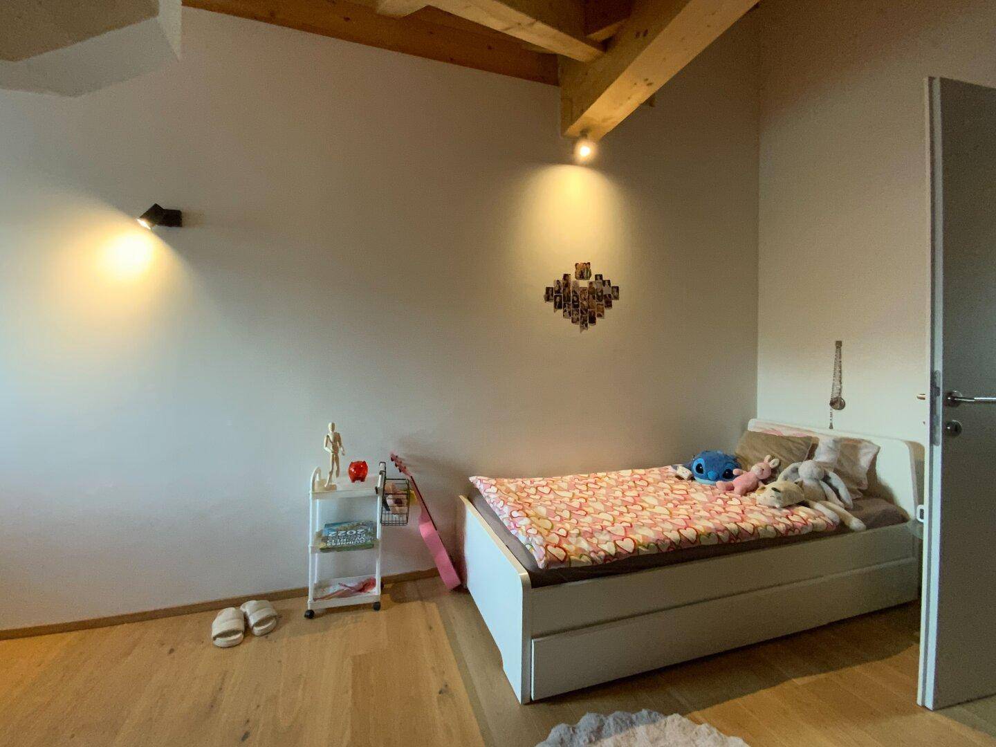 Helles Kinderzimmer mit Einzelbett, Holzbalkendecke und Dachschräge.