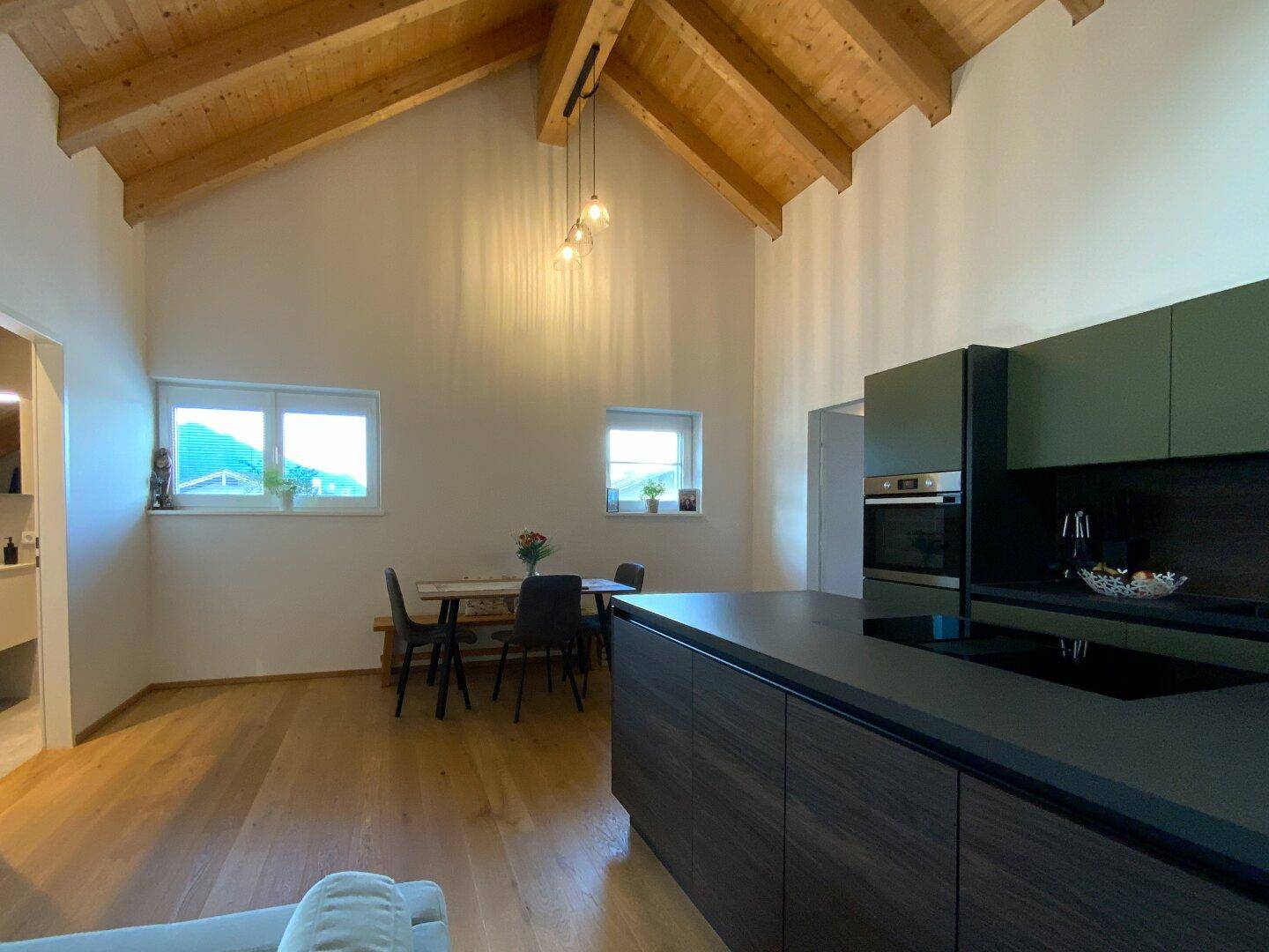 Heller Essbereich mit Holztisch und Blick auf die moderne Küche und die hohen Decken.