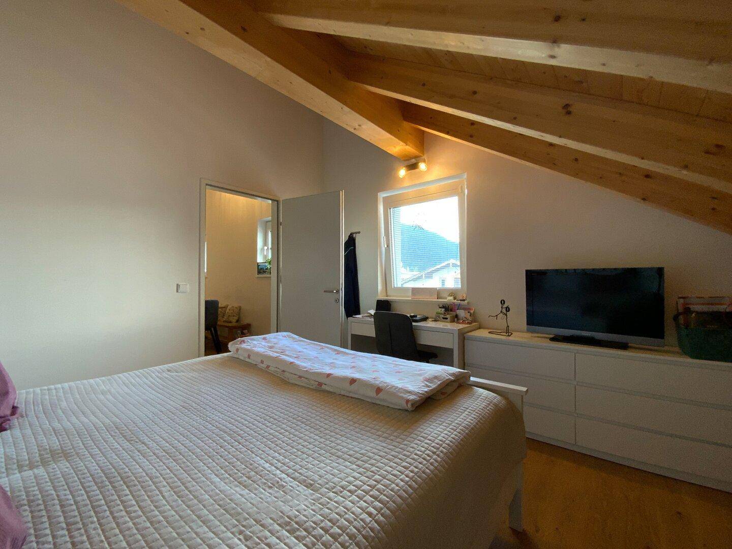 Schlafzimmer mit Doppelbett, Holzbalkendecke und Fenster mit Blick nach draußen.