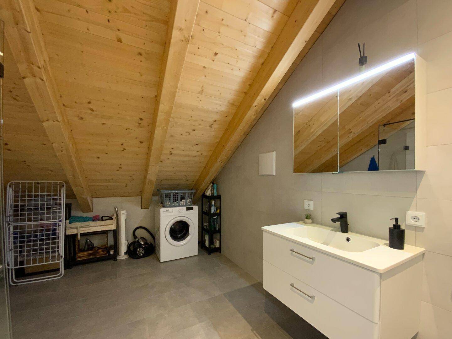 Modernes Badezimmer mit Dachschräge, Waschmaschine und Holzbalkendecke.