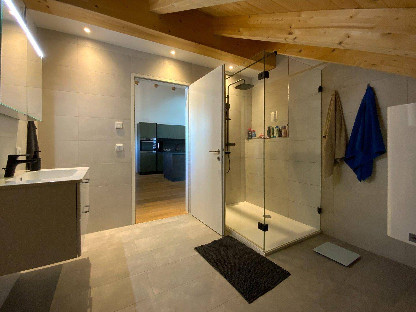 Modernes Badezimmer mit ebenerdiger Dusche, Waschtisch und Holzbalkendecke.
