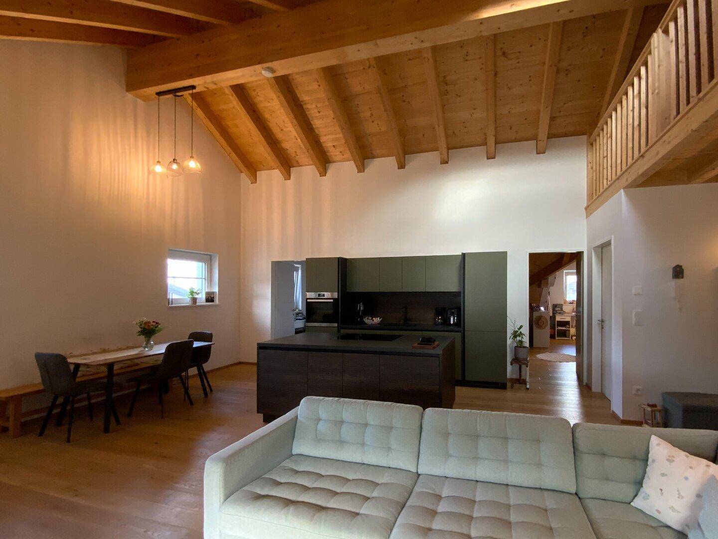 Geräumiger offener Wohnbereich mit Küche, Essplatz und gemütlichem Sofa unter Holzbalkendecke.