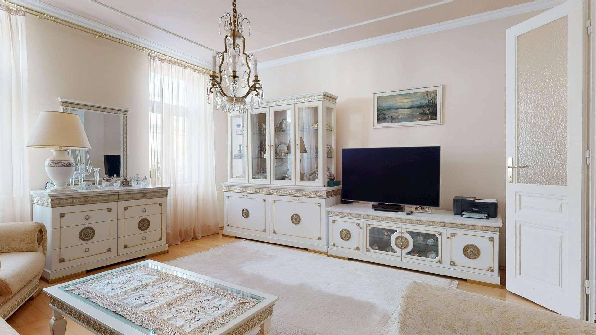 Elegantes Wohnzimmer mit klassischem Kronleuchter, hellen Möbeln und Holzboden.