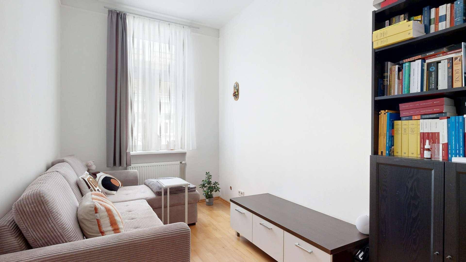 Einfaches Wohnzimmer mit Sofa, Bücherregal und hellem Holzboden.