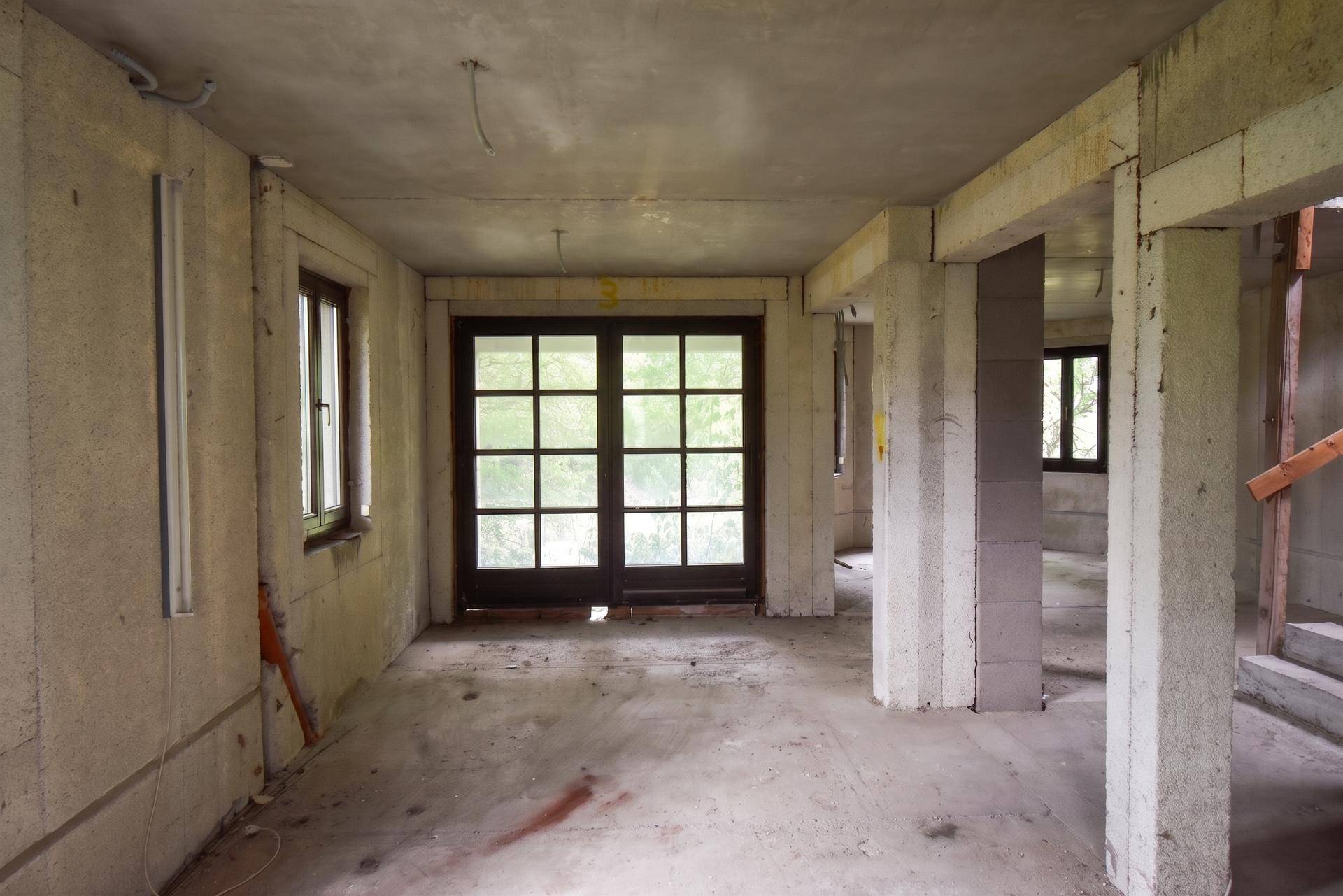 Rohbau-Innenraum mit großen Fenstertüren und Betonstützen, bereit für den Ausbau.