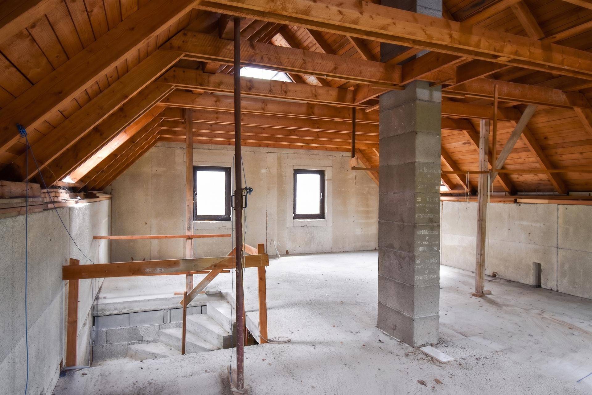 Geräumiger Dachboden im Rohbau mit sichtbaren Holzbalken und Dachfenstern.