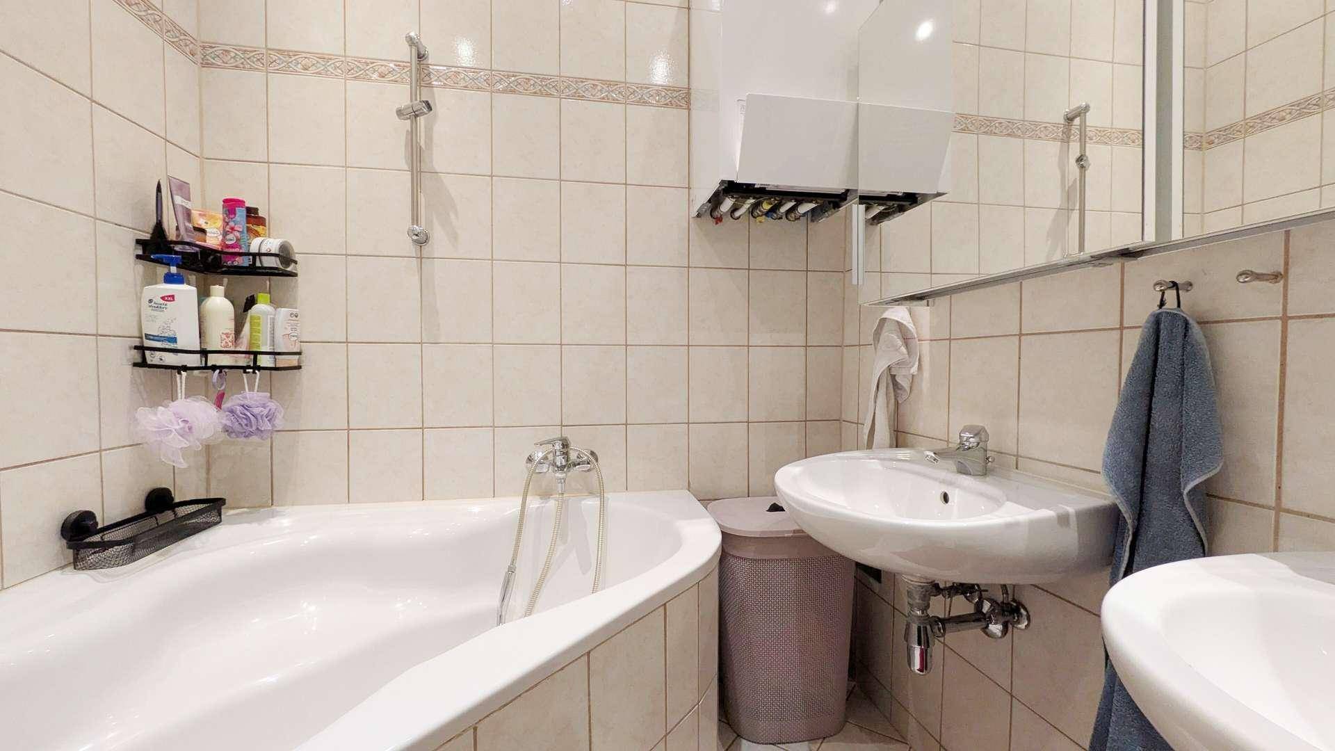 Gefliestes Badezimmer mit Badewanne, Waschbecken und Wandheizung.