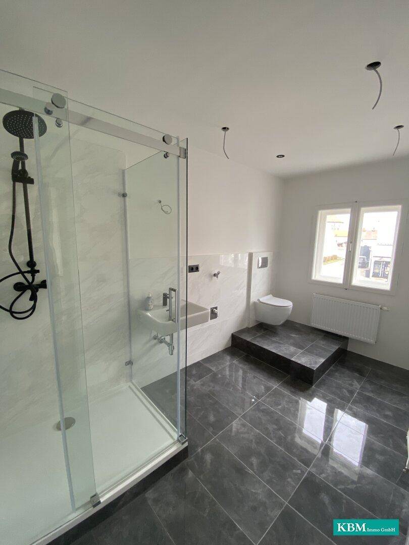 Modernes Badezimmer mit großer Duschkabine, dunklen Fliesen und wandhängendem WC für zeitgemäßen Komfort.