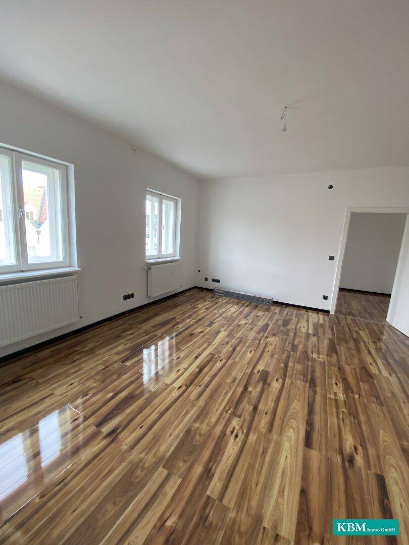 Leeres Wohnzimmer mit glänzendem Holzboden und weißen Wänden, bereit zur individuellen Gestaltung.