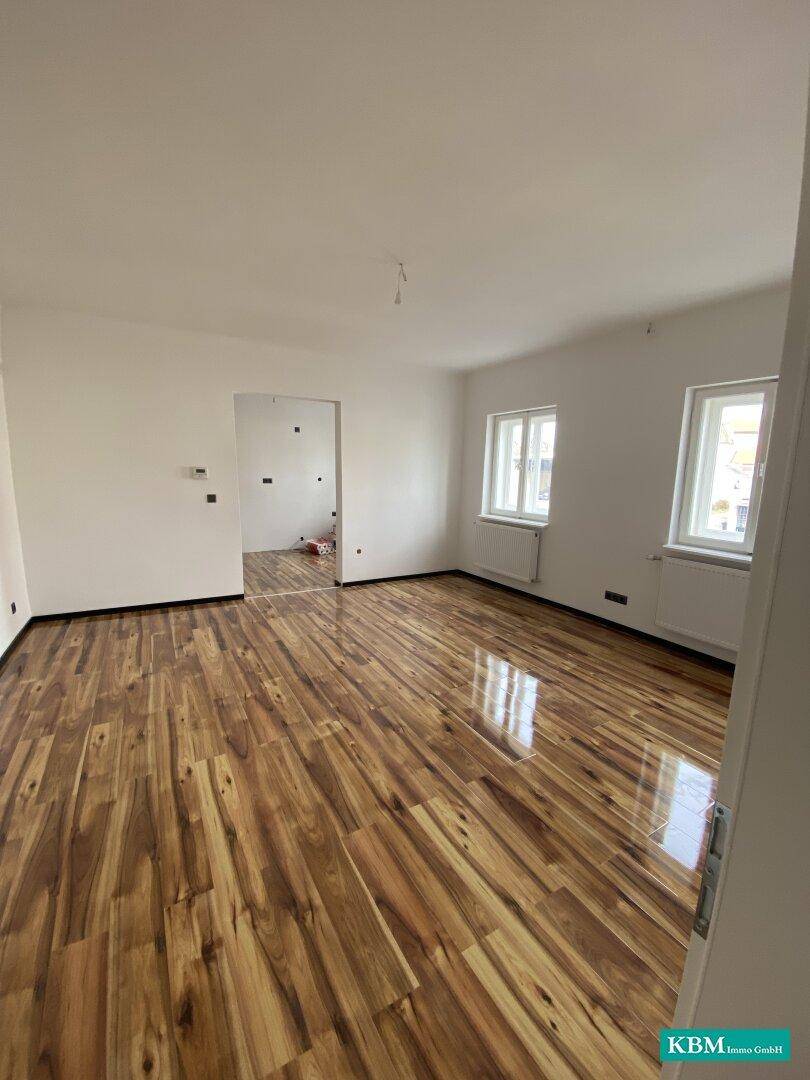 Heller, leerer Raum mit Holzboden und Fenstern, ideal für ein geräumiges Wohnzimmer.
