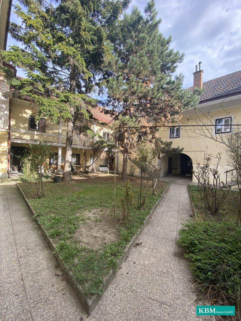 Grüner Innenhof mit Bäumen und Gehwegen, umgeben von historischen Gebäuden, bietet Ruhe.
