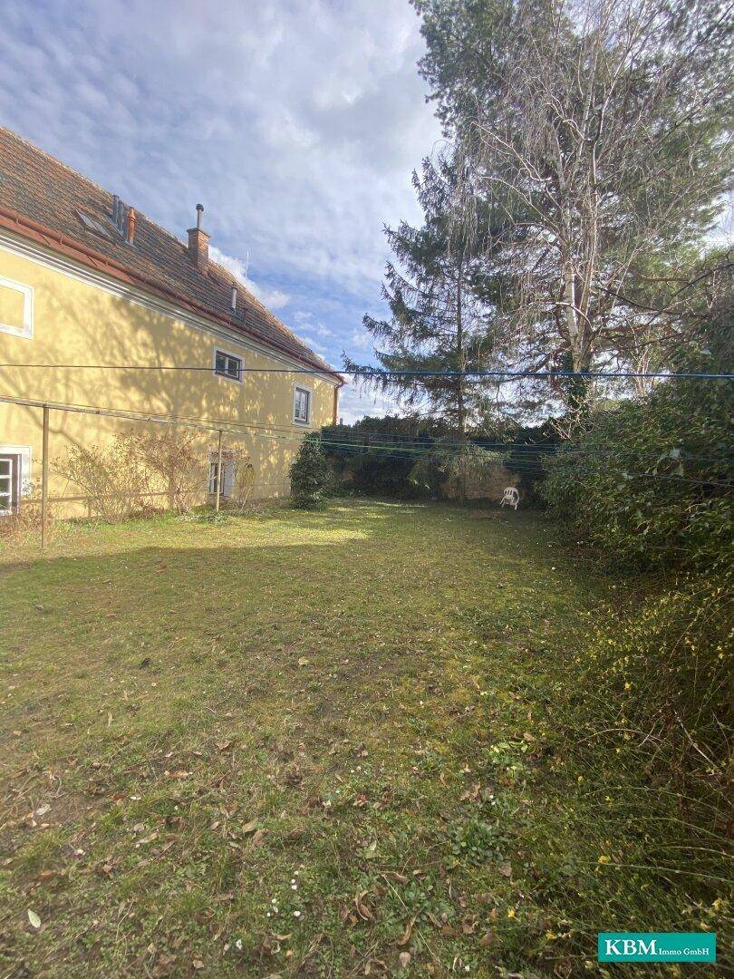 Großer Garten mit Rasenfläche und Blick auf die Rückseite eines historischen Gebäudes.