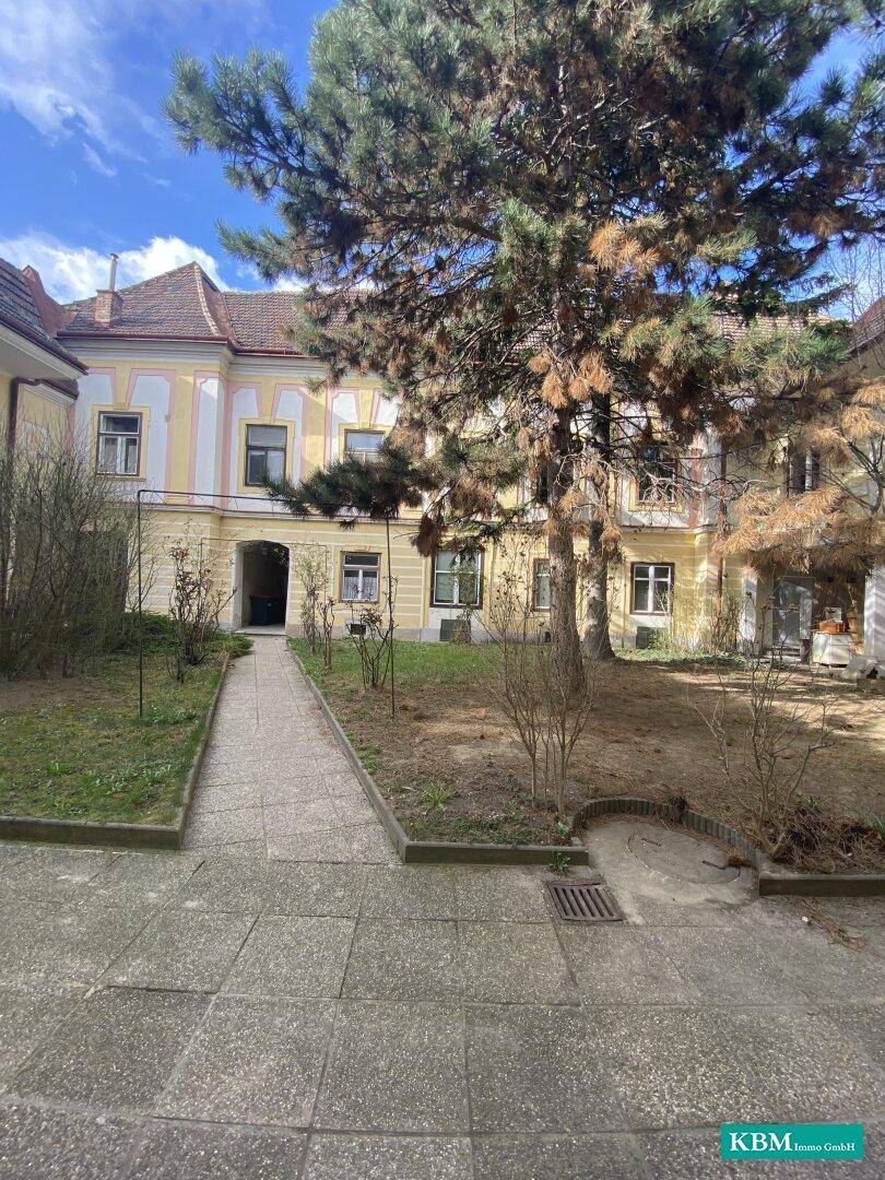 Innenhof mit Bäumen, Gehwegen und der Fassade eines historischen Gebäudes, einladend und gepflegt.