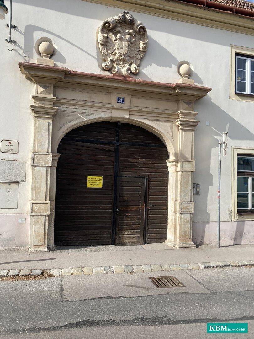 Historisches Gebäude mit einem großen, verzierten Torbogen und Wappen, das Eleganz ausstrahlt.