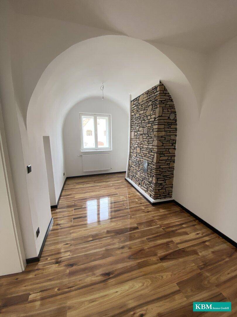 Heller Raum mit Gewölbedecke, Holzboden und markanter Steinwand, die ein besonderes Ambiente schafft.