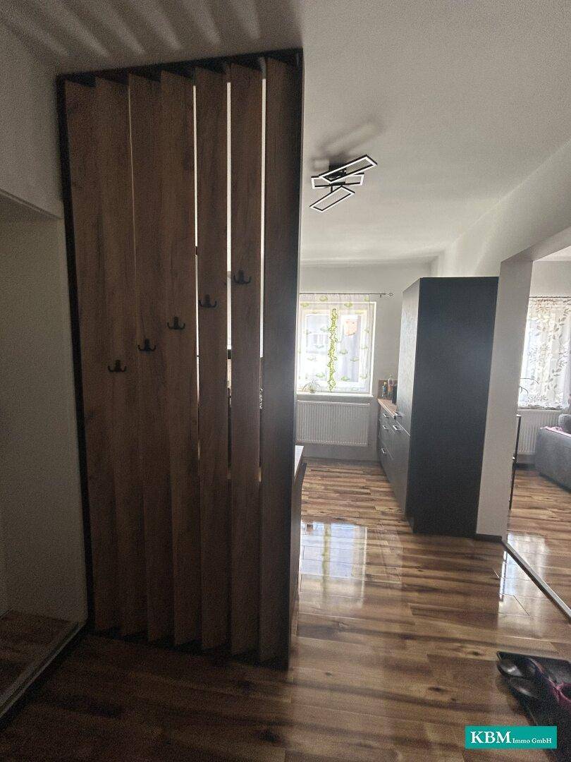 Eingangsbereich mit Holztrennwand und Garderobenhaken, die zum offenen Wohnbereich führt.