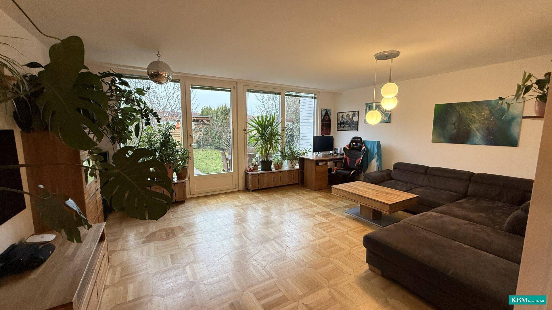 Gemütliches Wohnzimmer mit großem Sofa, Parkettboden und direktem Zugang zum Garten.