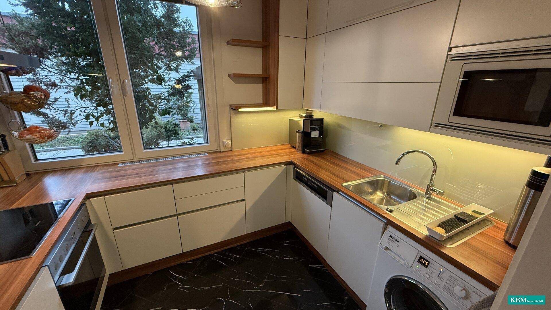 Funktionale Küche mit integrierten Geräten, Holz-Arbeitsplatten und Fenster mit Blick ins Grüne.
