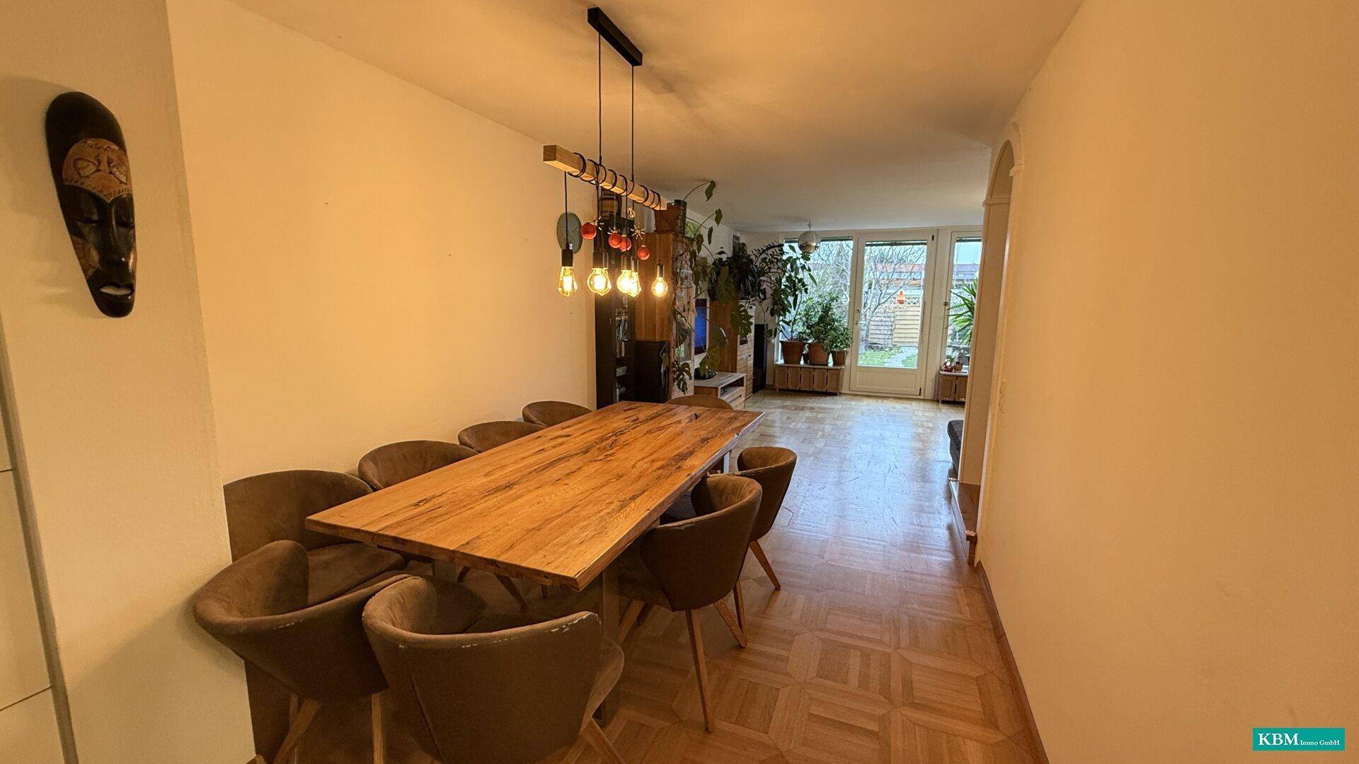 Geräumiger Wohn- und Essbereich mit Holztisch, Parkettboden und Blick in den Garten.