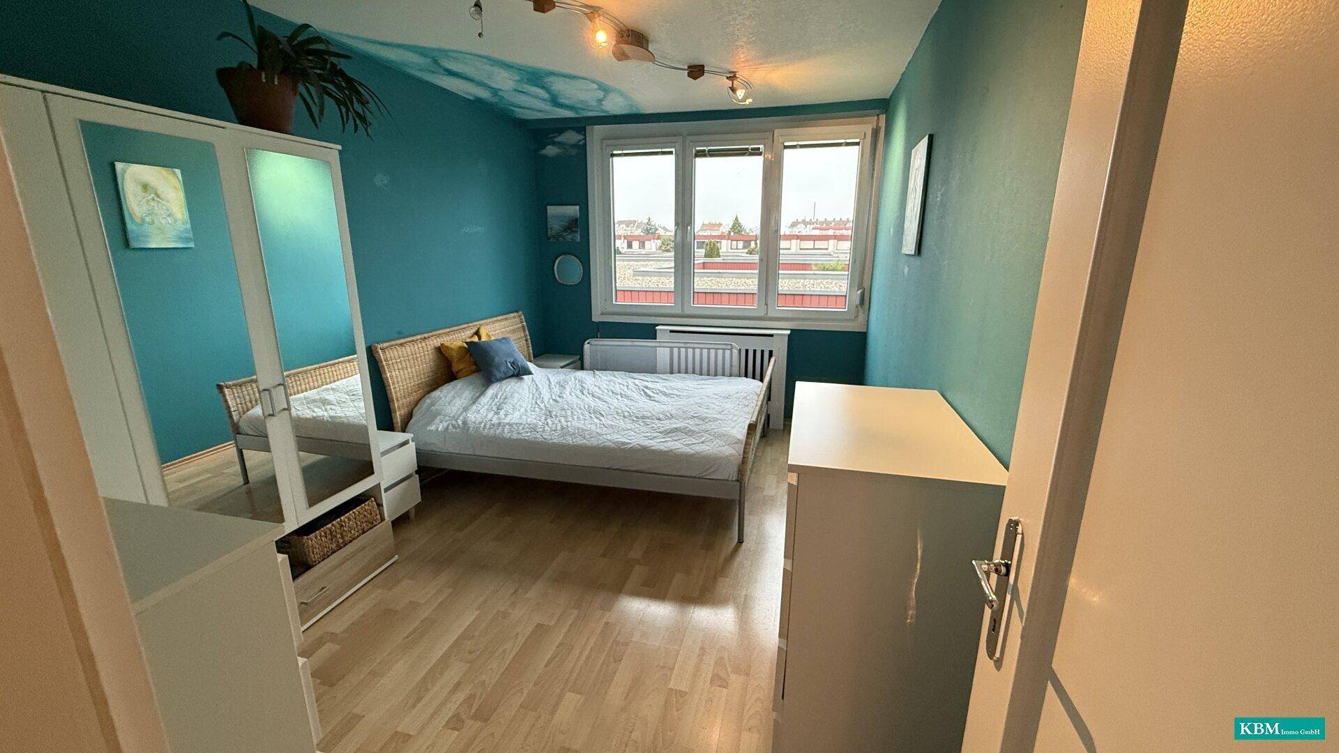 Schlafzimmer mit blau gestrichenen Wänden, Doppelbett und Fenster mit Stadtblick.
