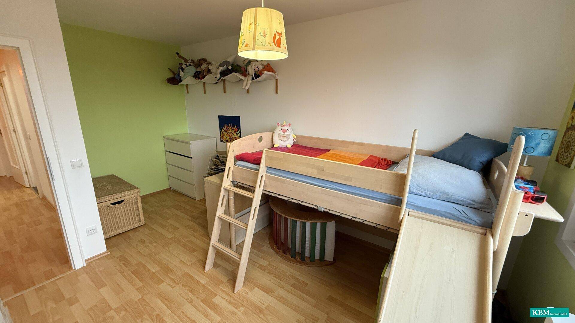 Kinderzimmer mit Hochbett, Rutsche, Laminatboden und grüner Akzentwand.