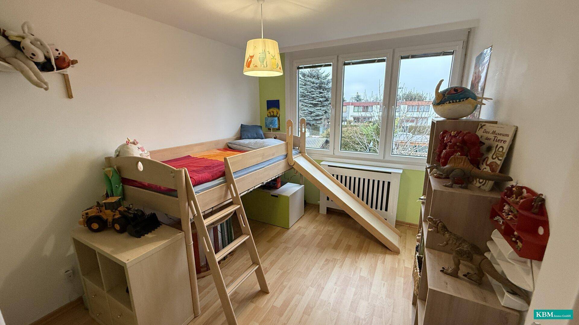 Helles Kinderzimmer mit Hochbett, Rutsche, Laminatboden und Blick ins Grüne.