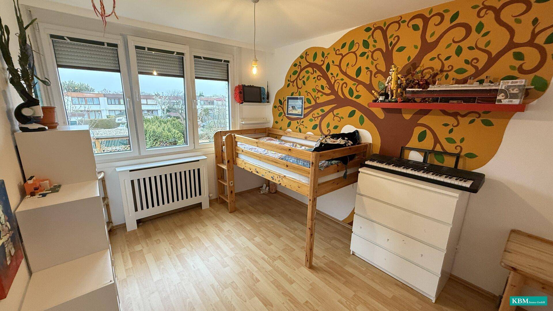 Kinderzimmer mit Hochbett, Laminatboden und kreativer Baumwandmalerei.