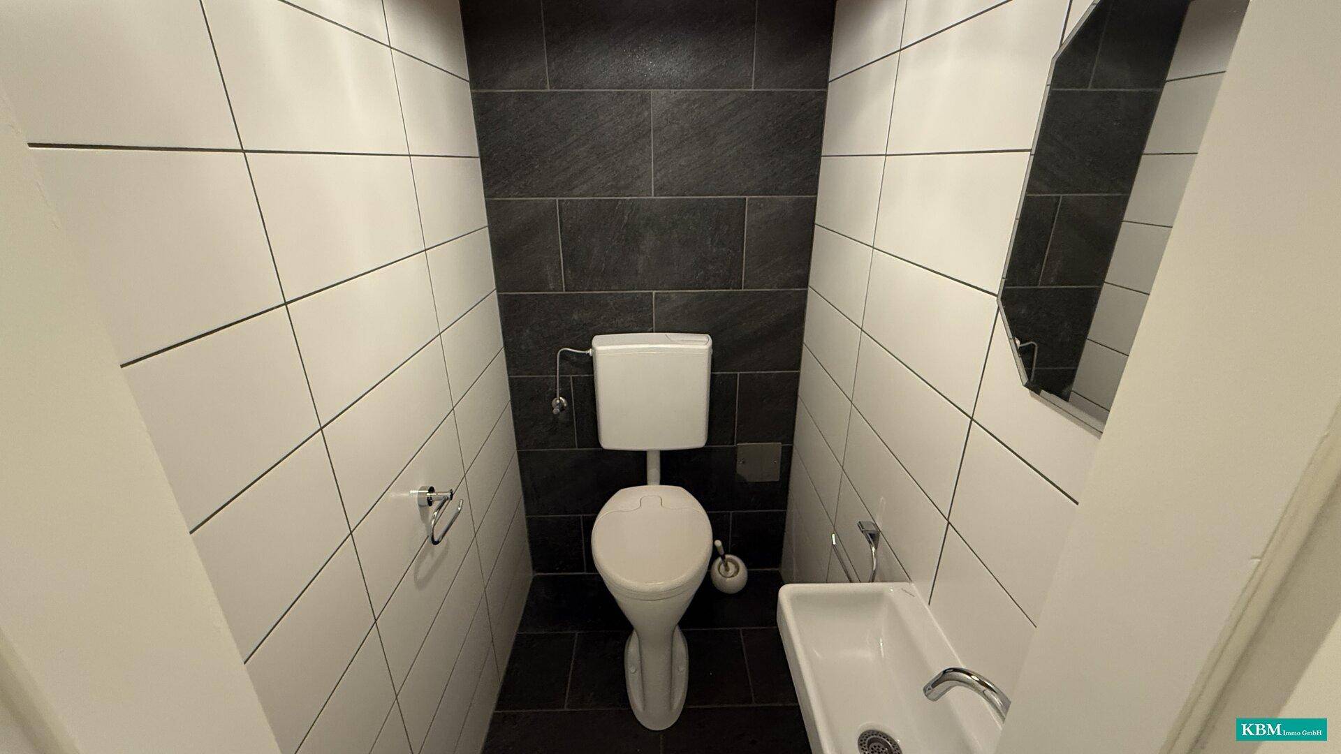 Kleines Gäste-WC mit Wand-WC, Waschbecken und modernen schwarz-weißen Fliesen.