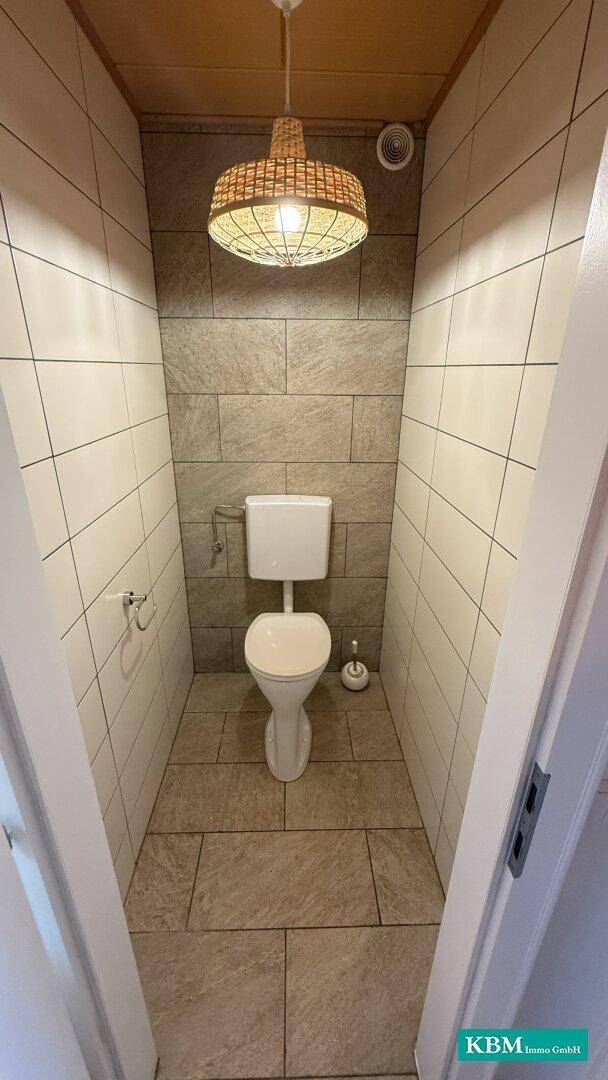 Modernes Gäste-WC mit Wand-WC, Steinoptik-Fliesen und Deckenleuchte.