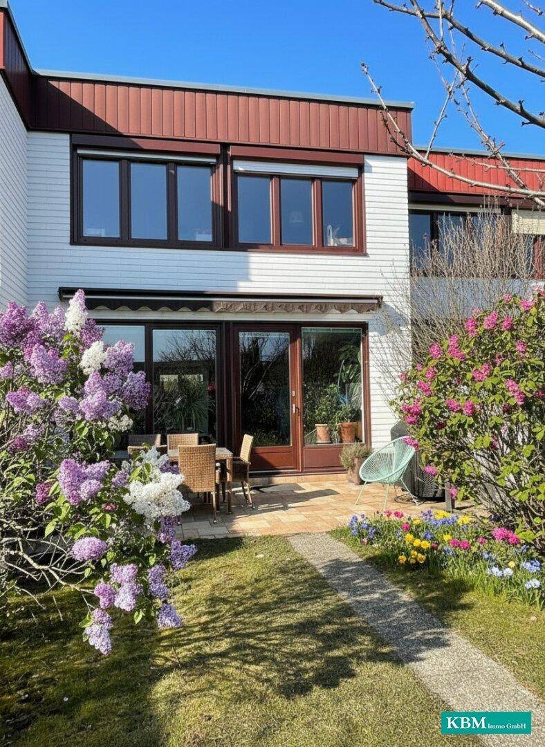 Hinterhof mit Terrasse, Gartenmöbeln und blühenden Sträuchern im Frühling.